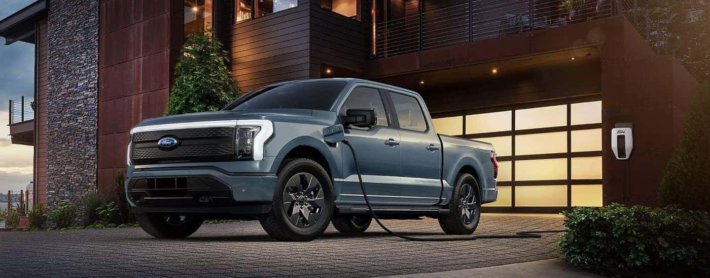 A light blue 2023 Ford F-150 Lightning plugged into a home charging station.