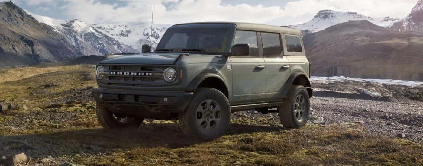A sage green 2023 Ford Bronco is parked off road in the mountains.
