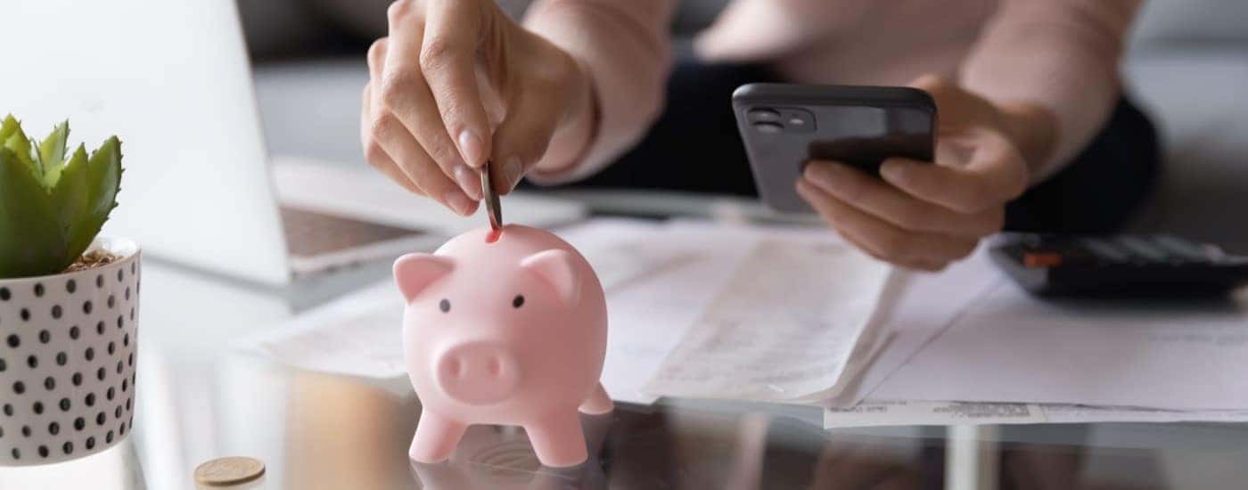 A person holding a phone and putting a quarter into a piggy bank