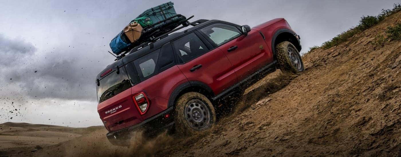 Red 2021 Ford Bronco Sport driving up a hill with camping gear on the roof rack.