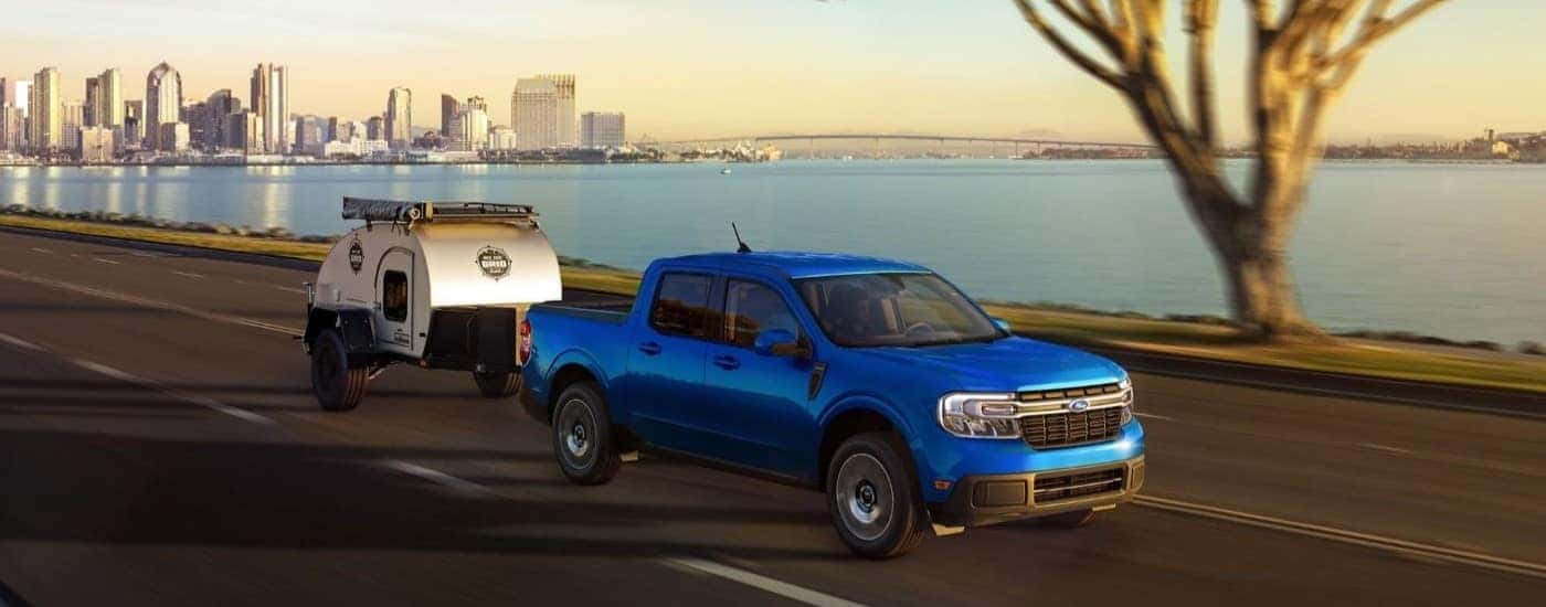 Blue 2023 Ford Maverick towing a pop-up camper along the water