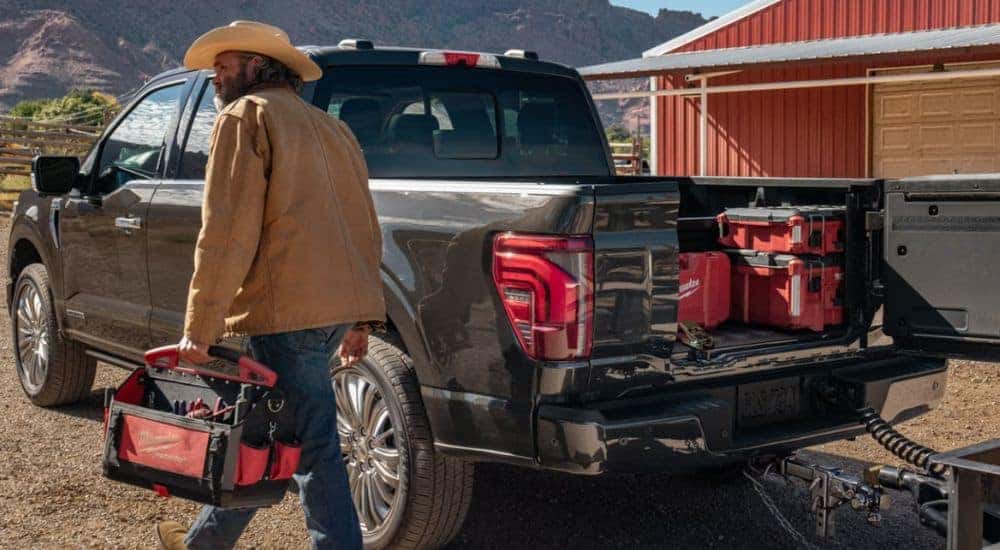 A man holding a tool box by a black 2026 Ford F-150 Platinum with Pro Access tailgate open.