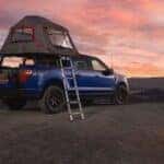 A person tending a fire next to a blue 2026 Ford F-150 STX FX4 with a tent accessory.