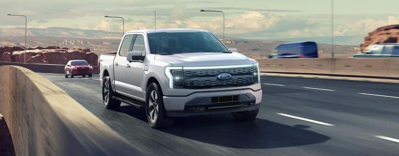 A silver 2023 Ford F-150 Lightning driving on a highway.