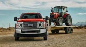 A red 2021 Ford F-Series Super Duty is shown from the front towing a red tractor.