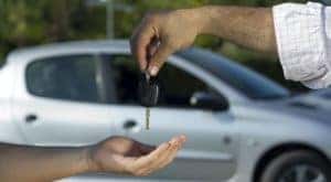 A salesman is passing a set of keys to a customer at a used car dealer in Shelbyville.