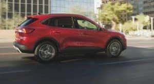A red 2021 Ford Escape is shown from the side while driving on a city street.