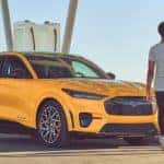 A yellow 2021 Ford Mustang Mach-E is shown parked next to a charging station.