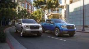 A silver and a blue 2022 ford Maverick are shown driving through a city.