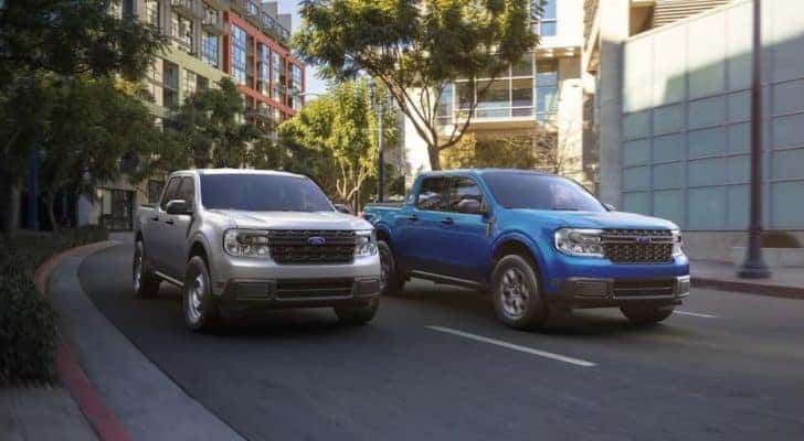 A silver and a blue 2022 ford Maverick are shown driving through a city.