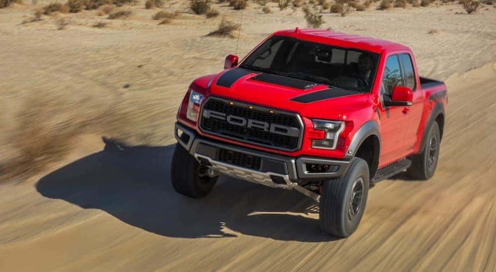 A red 2021 Ford F-150 Raptor is shown driving on a desert road after visiting a Lynchburg Ford F-150 dealer.