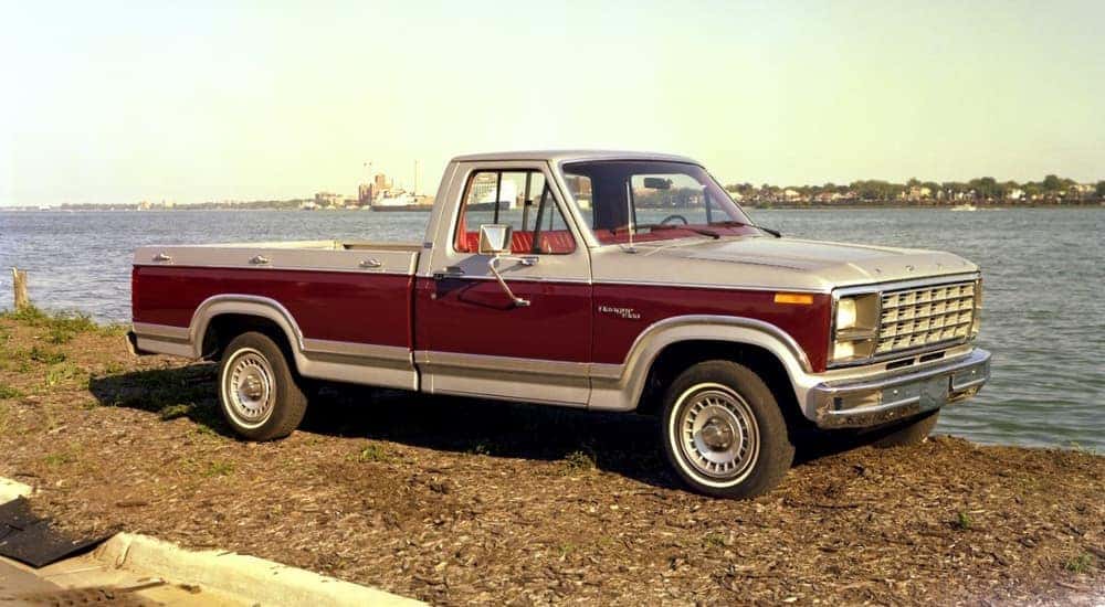 A red 1980 F-100 is shown parked next to a body of water.