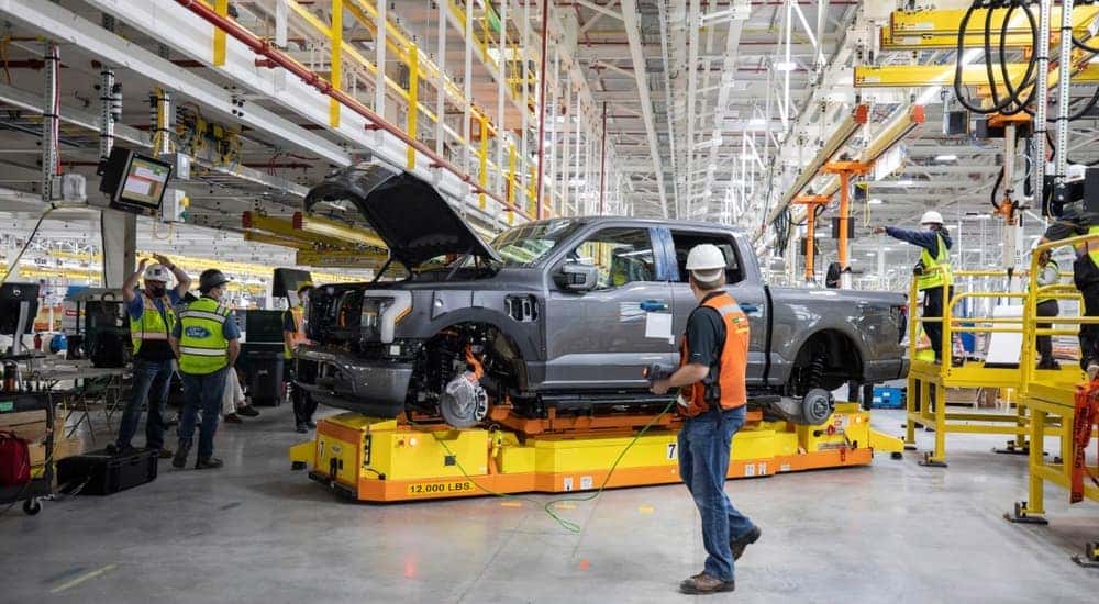 A grey 2022 Ford F-150 Lightning is shown being built at a factory.