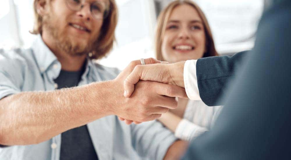 A customer is shown shaking hands with a salesman after discussing 'how to sell my car.'