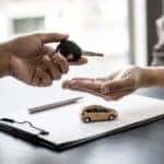 A customer is shown handing a car key to a salesman at a dealership.