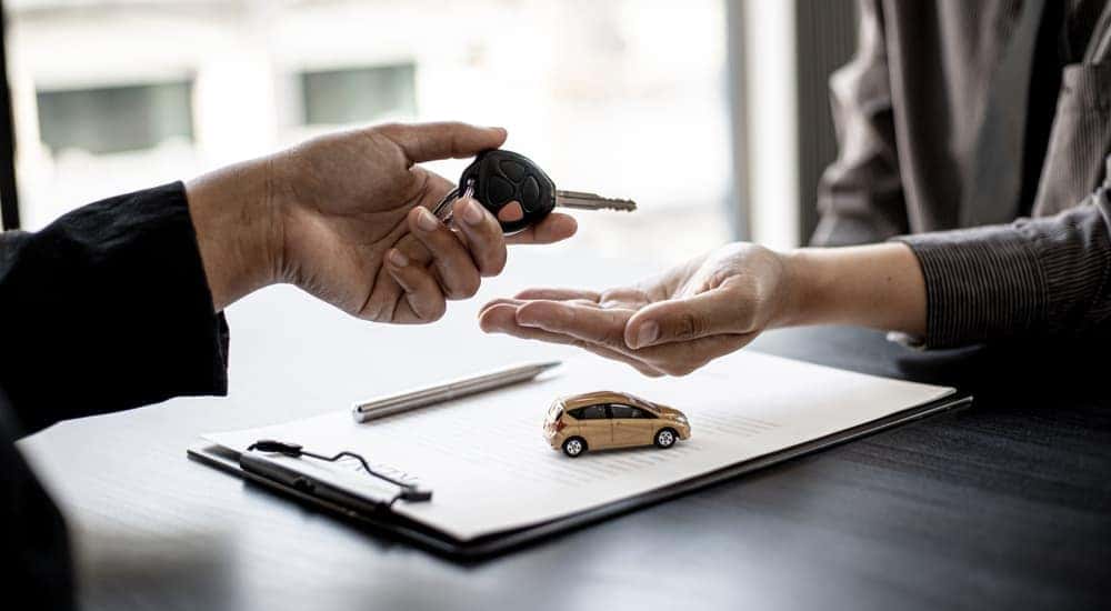 A customer is shown handing a car key to a salesman at a dealership.