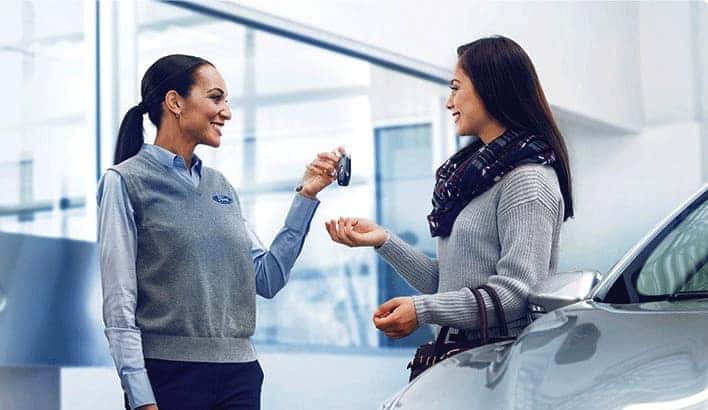 A saleswoman is shown speaking to a customer about certified pre-owned vehicles.