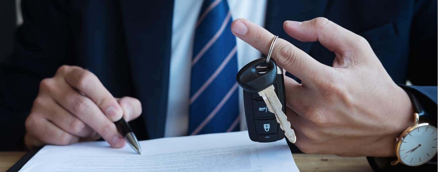 A salesman is shown holding a car key and filling out paperwork.
