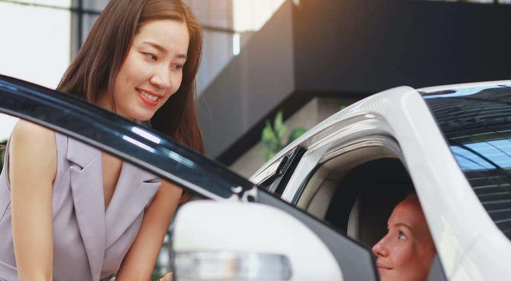 A salesperson is shown helping a customer look at a certified pre-owned vehicle.