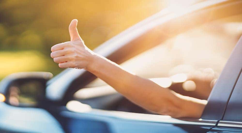 A person is shown giving a thumbs up as they drive away in a certified pre-owned vehicle.