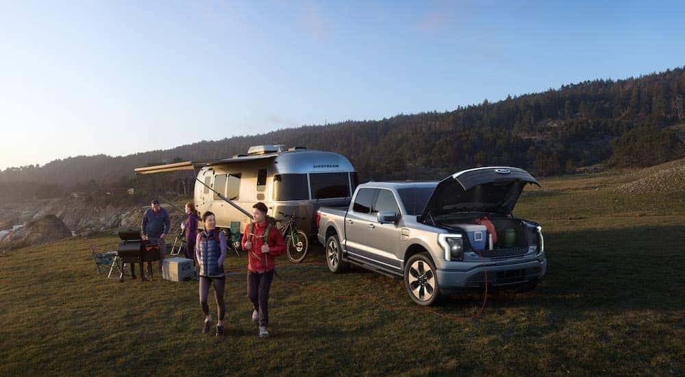 A silver 2022 Ford F-150 Lightning Platinum is shown at a campsite with an Airstream trailer.