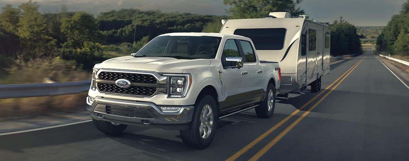 A white 2022 Ford F-150 is shown towing a camper down a highway.