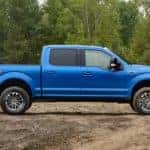 A blue 2019 Ford F-150 is shown from the side parked on a dirt clearing.