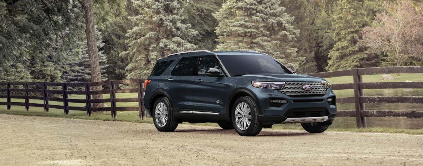 A blue 2023 Ford Explorer is shown parked in a field next to a fence.