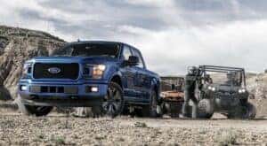 A blue 2020 Ford F-150 is shown parked next to two UTVs.
