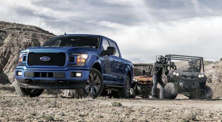A blue 2020 Ford F-150 is shown parked next to two UTVs.