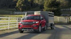 A red 2023 Ford Explorer is shown towing a trailer on a farm.
