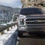 A grey 2021 Ford F-150 is shown from the front driving on an open road.