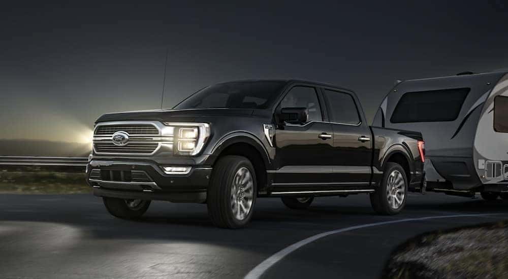 A black 2021 Ford F-150 is shown towing a trailer after leaving a certified ford truck dealer.