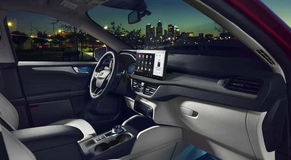 The black and grey interior of a 2023 Ford Escape with infotainment screen and nighttime cityscape outside