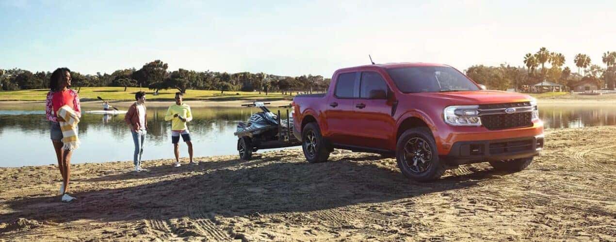 A red 2023 Ford Maverick is shown next to a lake towing jetskis.