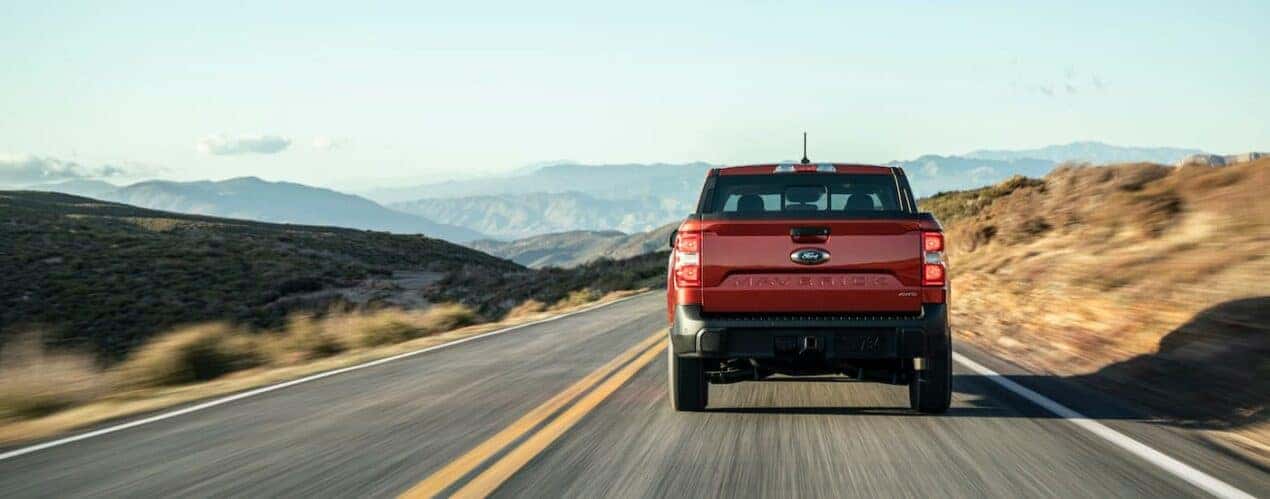 A red 2023 Ford Maverick Lariat is shown from the rear driving on an open road.