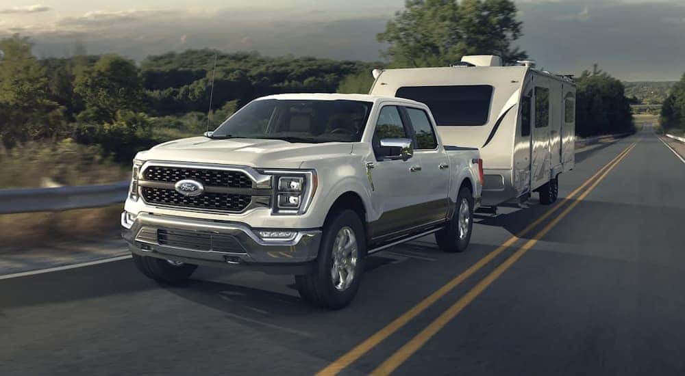 A white 2023 Ford F-150 towing a trailer on an open road.