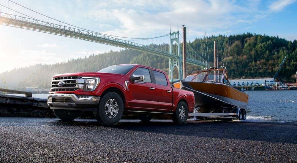 A red 2022 Ford F-150 Lariat is shown towing a boat out of a lake.