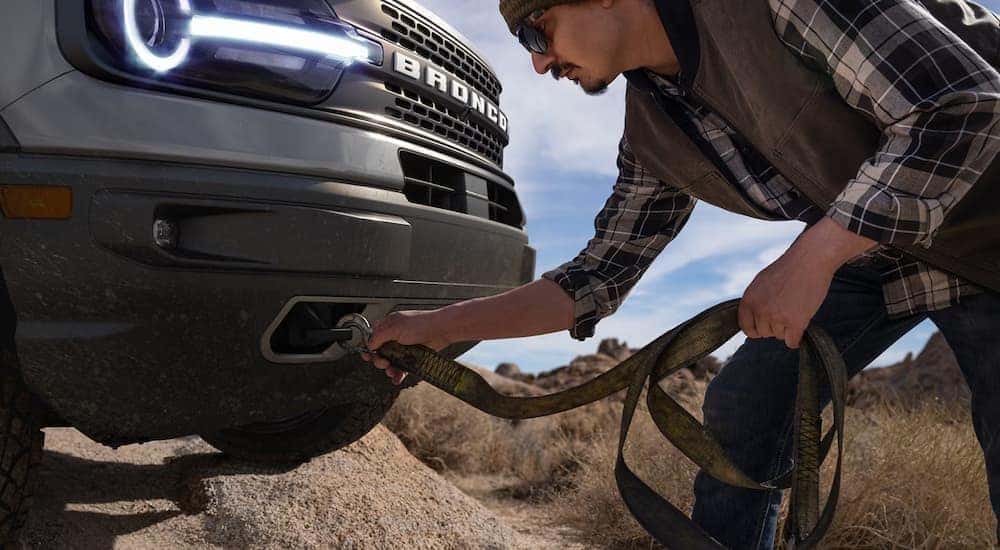 A person is shown attaching straps to tow hooks on a grey 2023 Ford Bronco Sport.