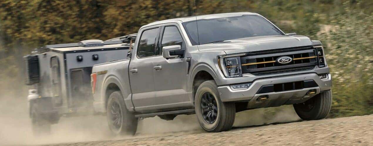 A grey 2023 Ford F-150 Tremor is shown towing a smaller camper trailer on a dusty road.