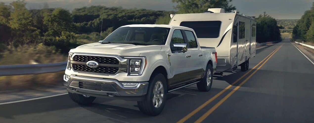 A white 2023 Ford F-150 is shown towing a camper trailer during a 2023 Ford F-150 vs 2023 Chevy Silverado 1500 comparison.