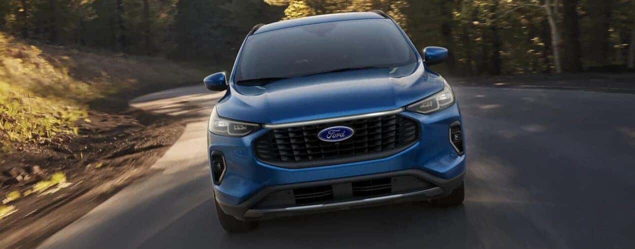 A blue 2023 Ford Escape is shown from the front driving on a winding road.
