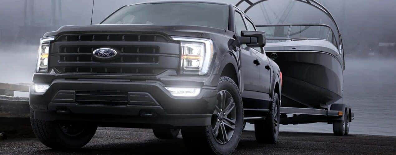 A black 2023 Ford F-150 is shown towing a boat on a foggy road.