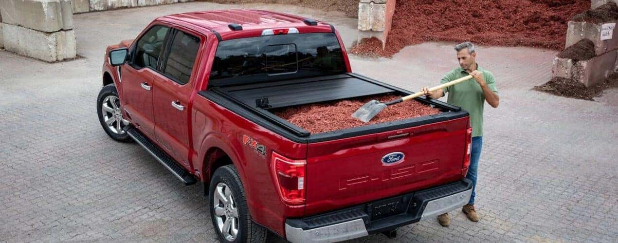 A man is shown loading mulch into the bed of a red 2023 Ford F-150.