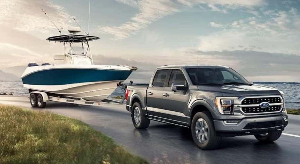 A silver 2023 Ford F-150 Lariat is shown towing a boat near a lake.
