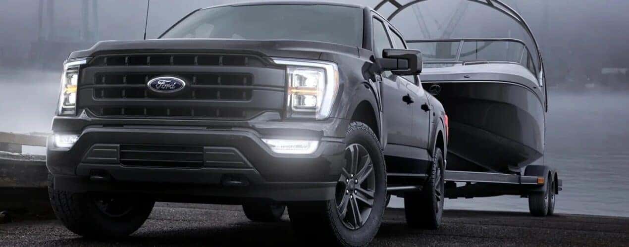 A black 2023 Ford F-150 is shown from the front while towing a boat.