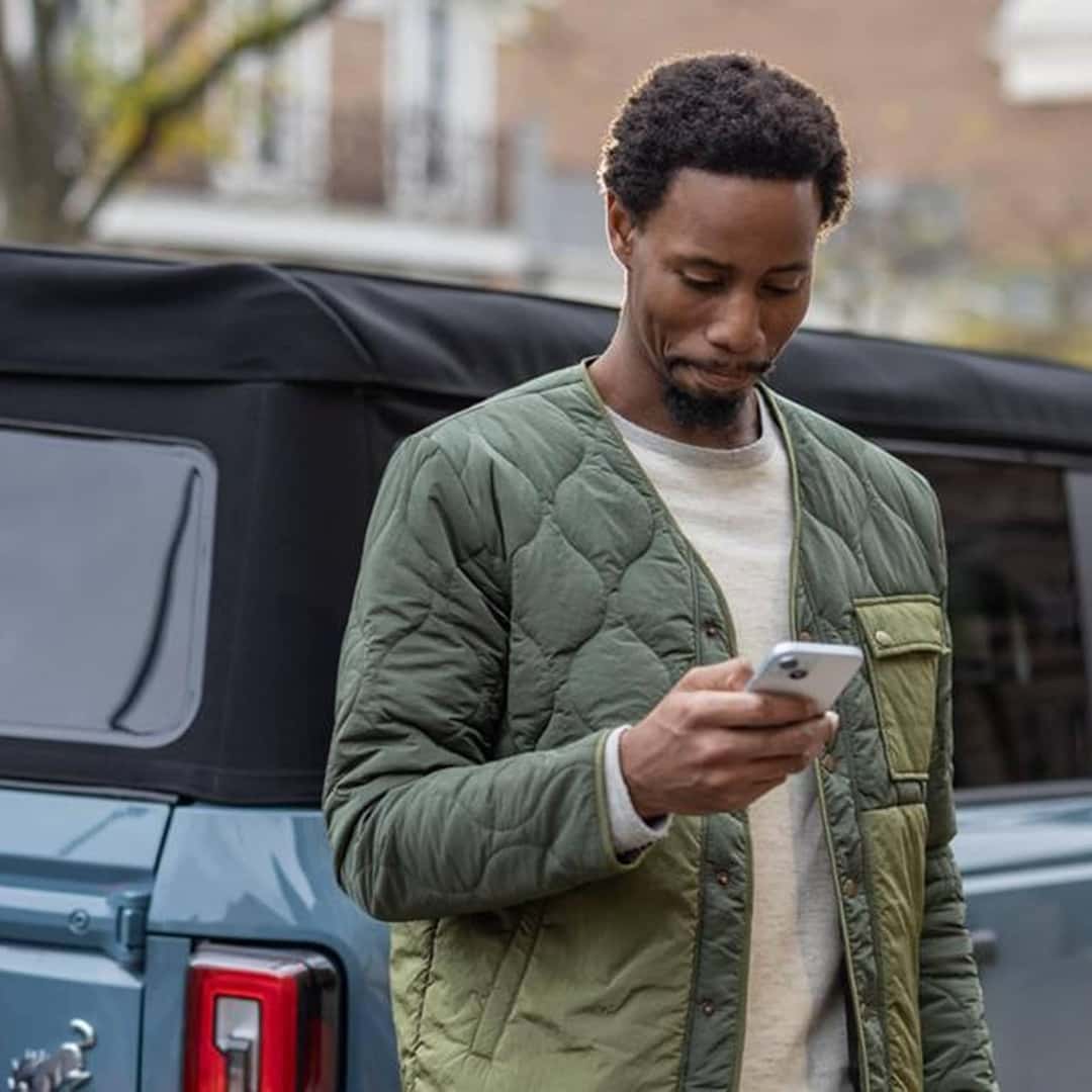man looking at phone next to bronco