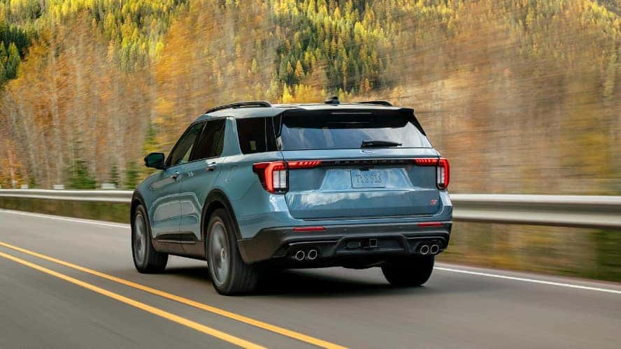 A blue Ford Explorer driving on the road near a forest.