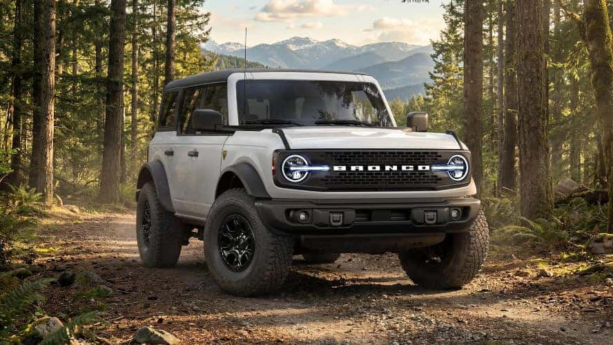 A silver Ford Bronco driving off-road through a forest.