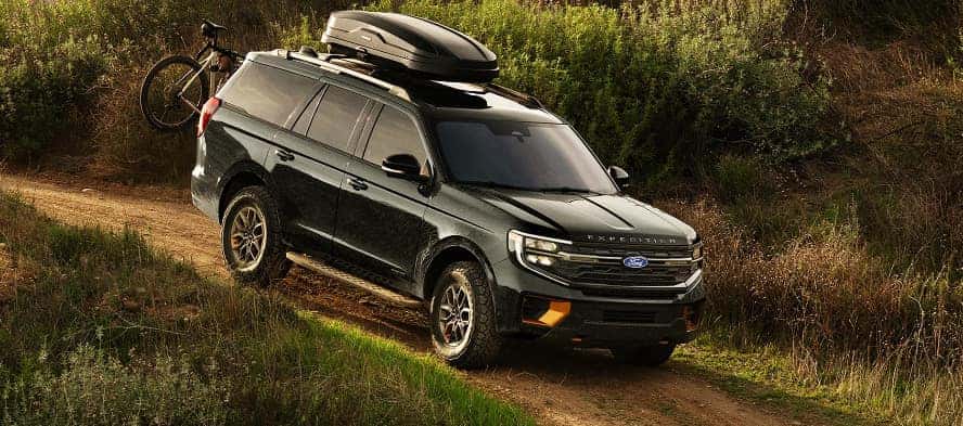 A black Ford Expedition driving down a dirt road incline with a bike attached to the trunk.